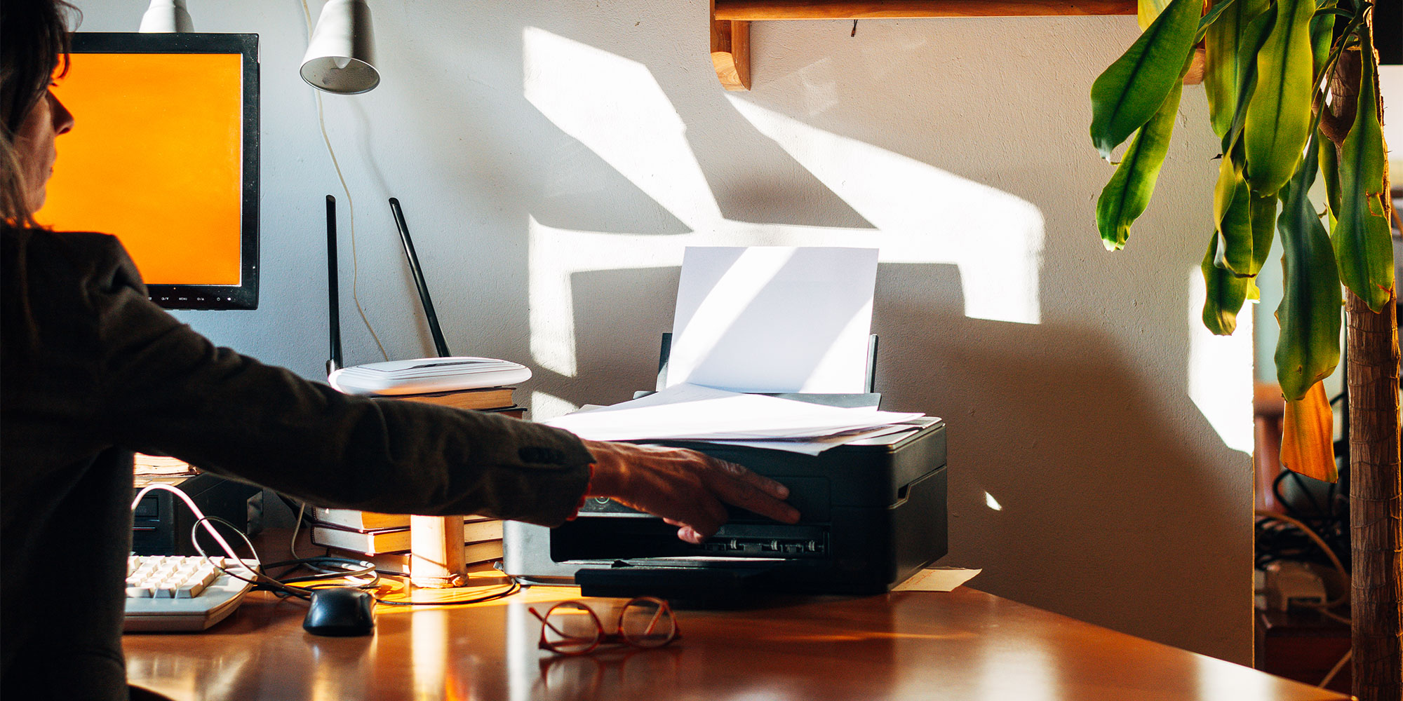 A hand adjusts the control panel of a printer while it outputs a colorful document featuring text and images.