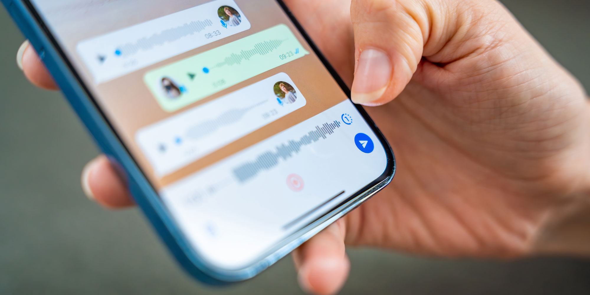 A hand holding a smartphone displaying voice messages with waveform visualizations and play buttons.