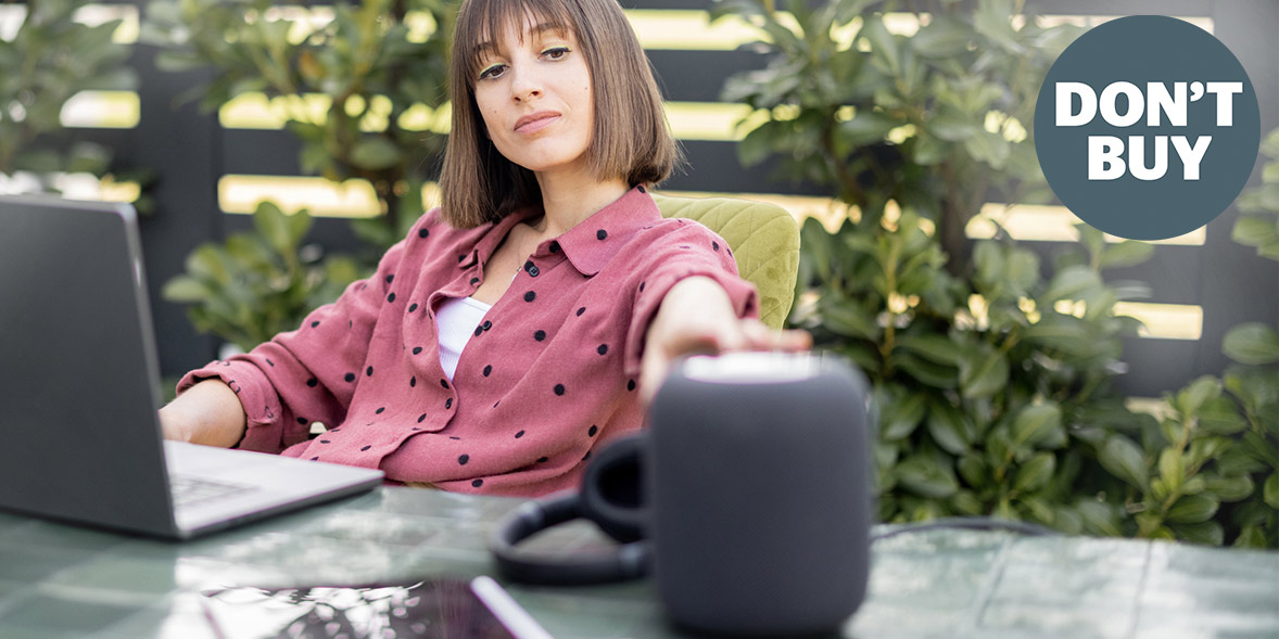 A woman with shoulder-length hair in a pink polka dot shirt reaches towards a speaker while sitting at a table outdoors.