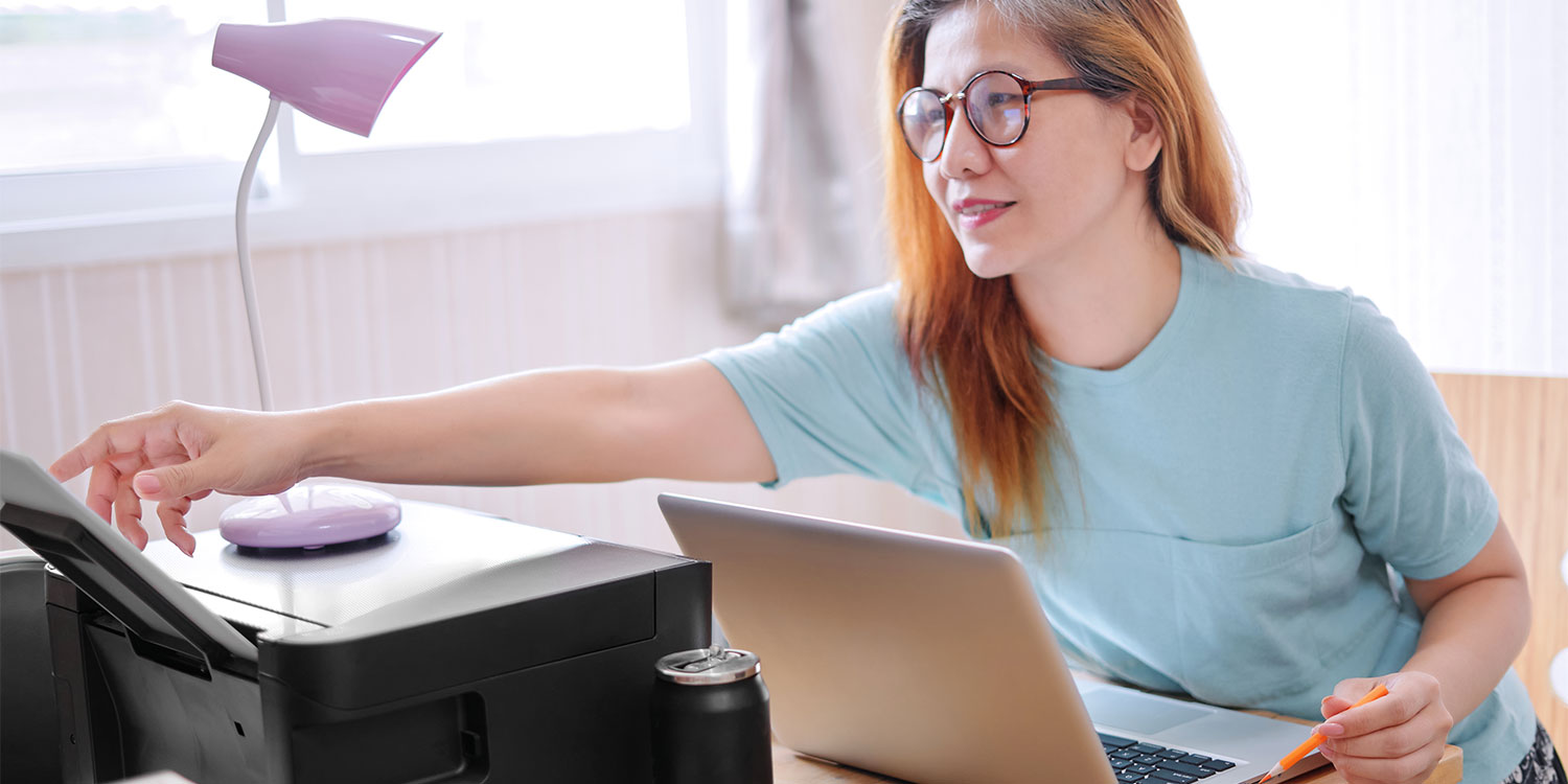 Man in a light blue shirt placing colorful document pages in a printer, focused on his task in a cluttered office environment