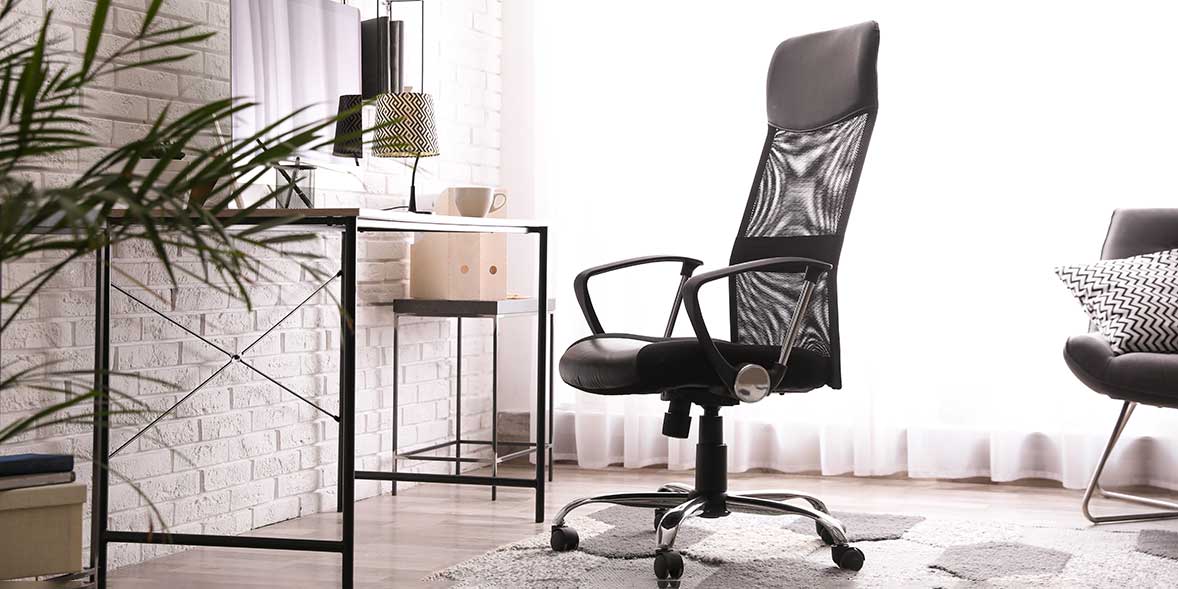 Ergonomic black office chair with mesh back near a modern desk, surrounded by light curtains and a potted plant.