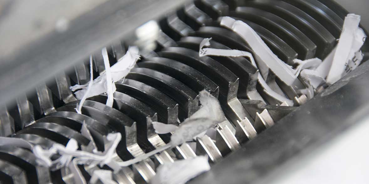 Close-up of a paper shredder's metal blades with shredded paper pieces scattered among the sharp edges.