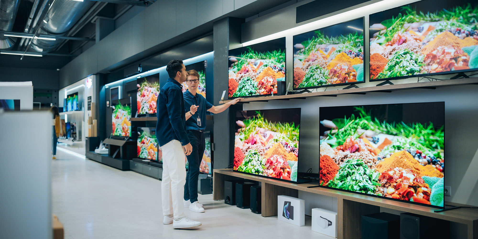 A man is browsing a large TV selection in a store.