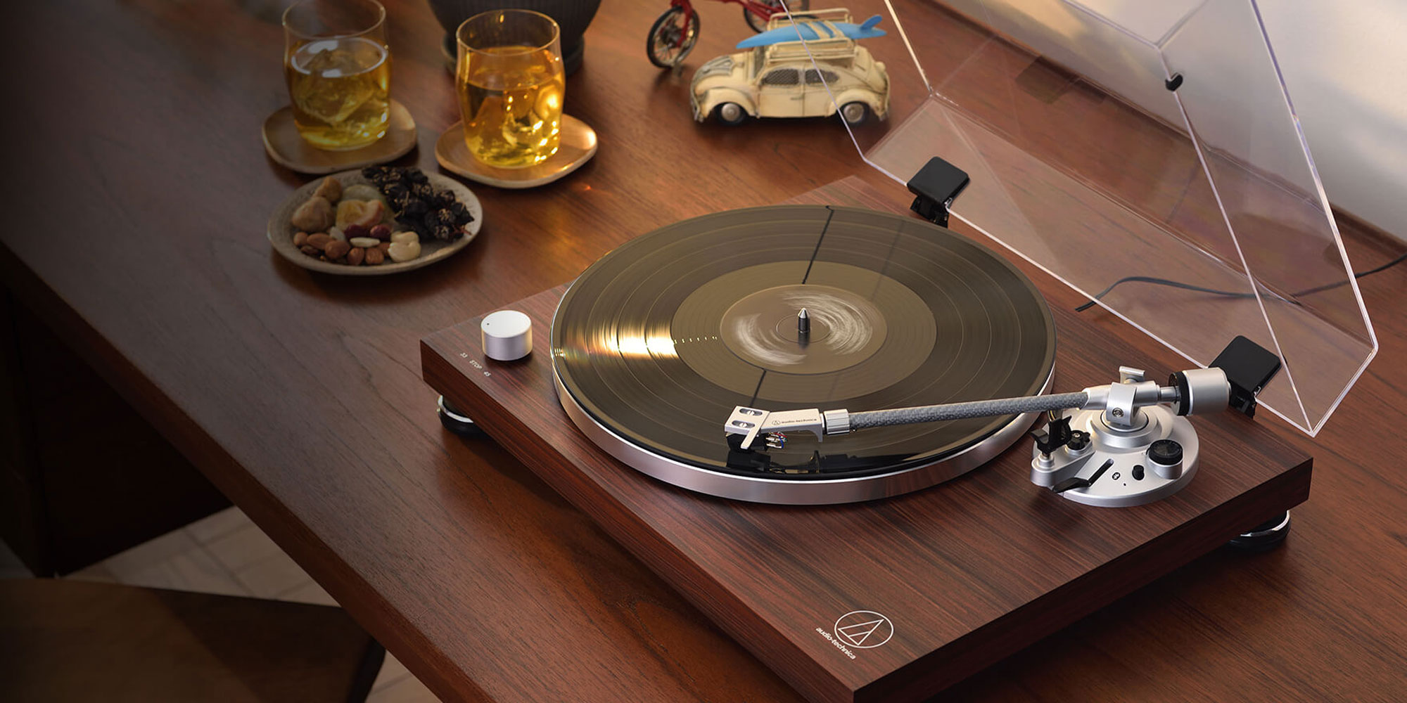 Stylish turntable on a wooden table, playing a record, with two glasses of yellow drink and a plate of nuts beside it.