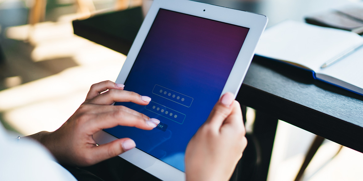 Hands holding a white tablet with a blue gradient screen displaying password fields, set on a wooden table.