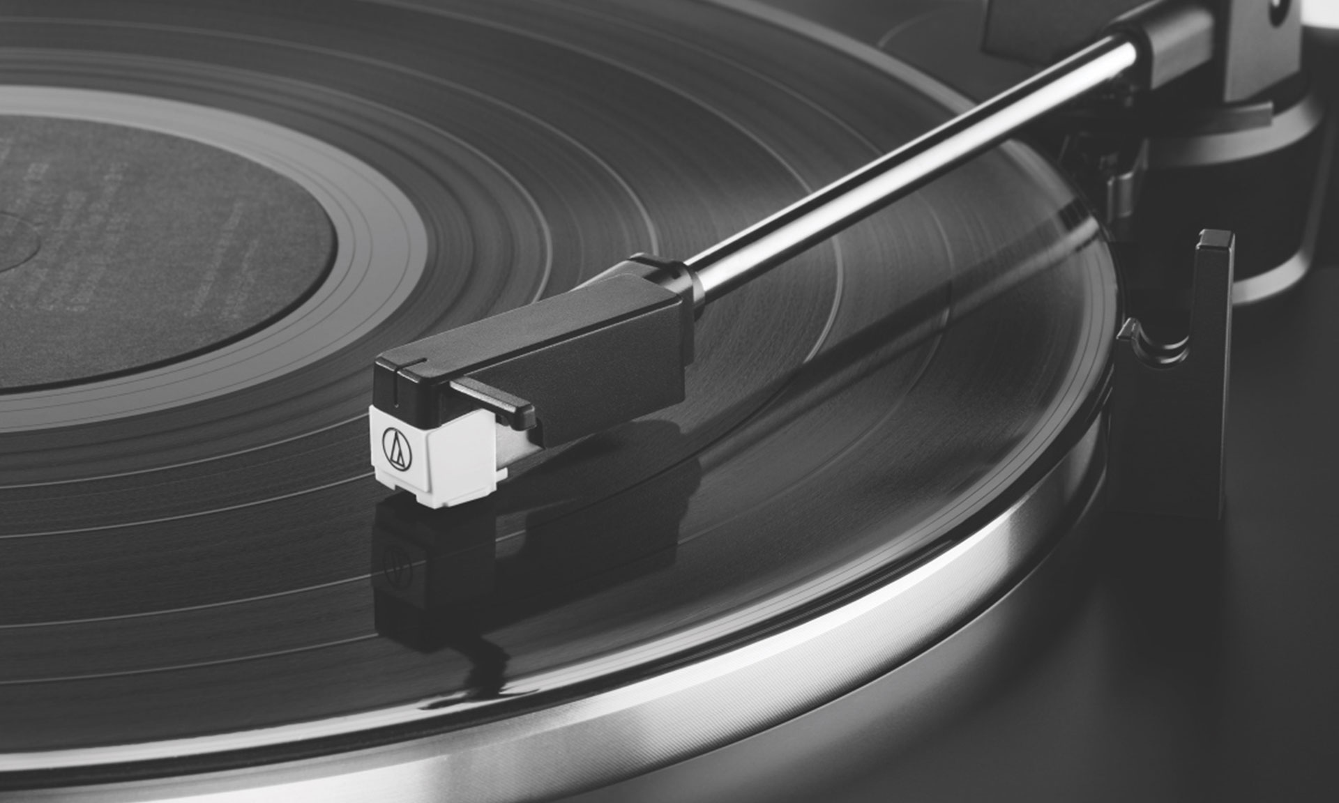 Close-up of a vinyl record on a turntable, with the tonearm and stylus resting on the record's surface.