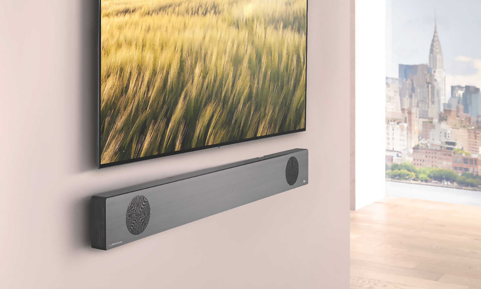A sleek soundbar mounted under a television, with a blurred image of golden grass and a city skyline in the background.