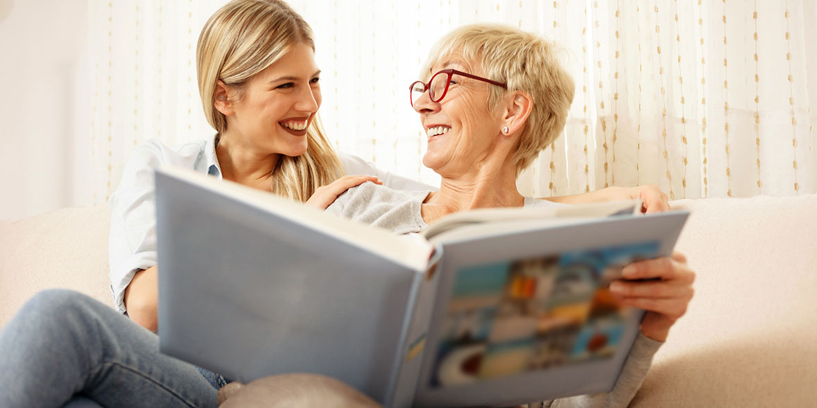A young and older woman smile together looking at a book