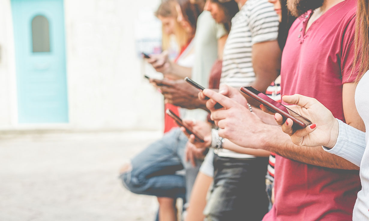 A group of people standing in a row, all looking at their smartphones, with a blurred background featuring a blue door.