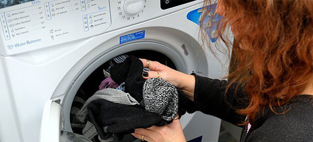 A person with reddish-brown hair holds a bundle of dark socks near a washing machine door.